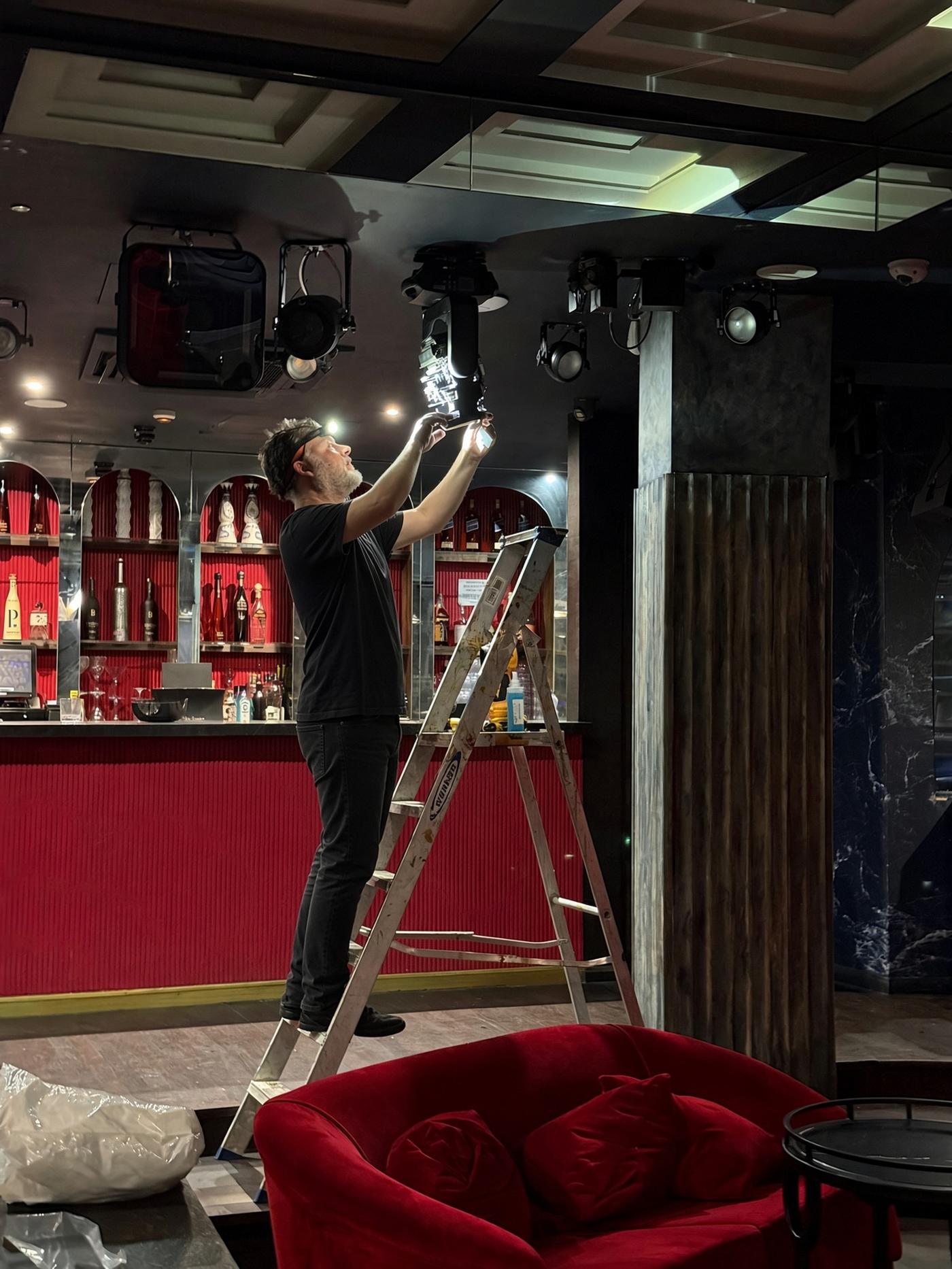 An SSB engineer up a ladder servicing a lighting fixture above the bar