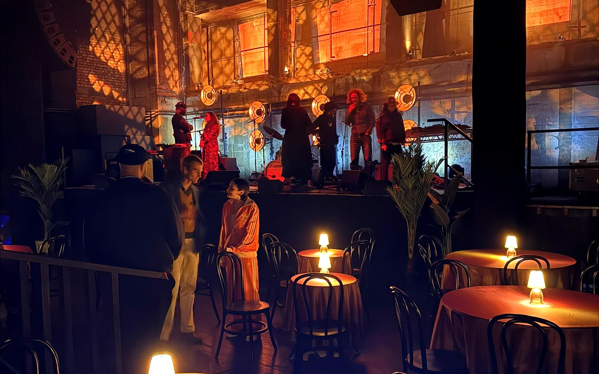 A lit stage and warm table lamps across a venue floor